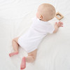 Minnie Me Cotton Romper Neutral, a baby lying on a white surface wearing a white romper and playing with a wooden toy.