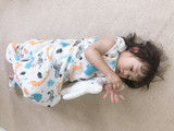 Karitree Four Layer Jungle Sleeveless Sleeping Bag, baby girl lying on a beige carpet with a colorful jungle animal print, holding a plush toy.