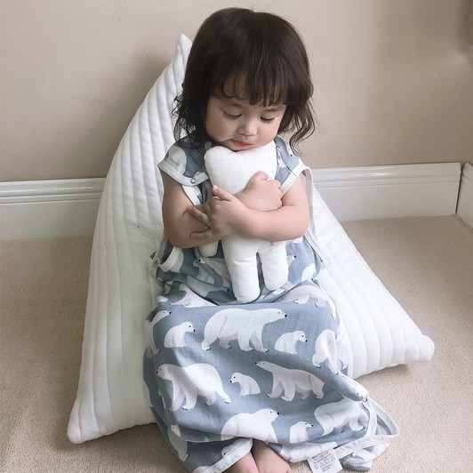 Karitree Double Layer Polar Bear Sleeveless Sleeping Bag, a child sitting on the floor holding a plush polar bear toy, with a white pillow behind her, wearing a polar bear patterned sleep sack.
