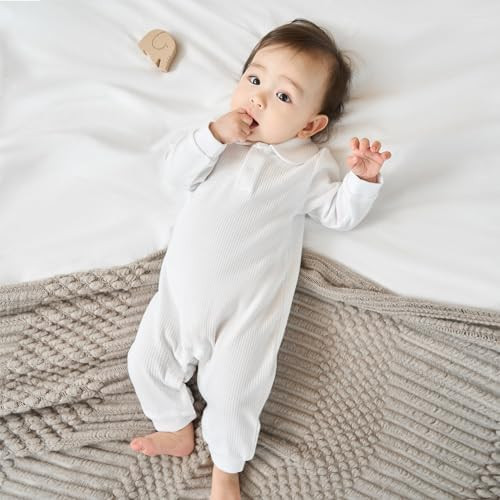 Minnie Me White Cotton Ribbed Romper, a baby lying on a bed wearing a white ribbed romper with a soft knitted blanket underneath.