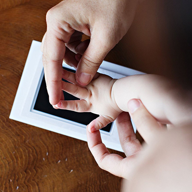 Generic Foot and Hand Print Clean Touch Ink Pad, demonstrating a parent using the ink pad to make a footprint or handprint on paper with a child's hand.