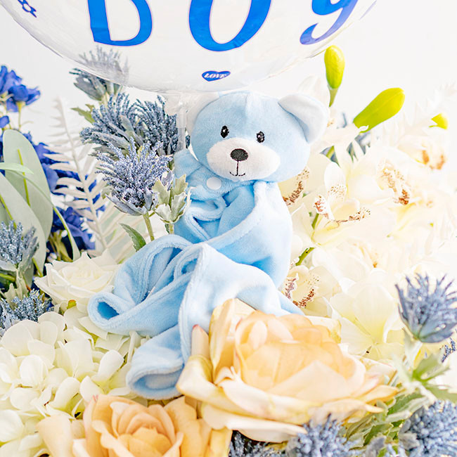Generic Gift Box Bear Comforter And Blanket Blue, blue stuffed bear comforter and blanket surrounded by white and purple flowers with a balloon in the background.
