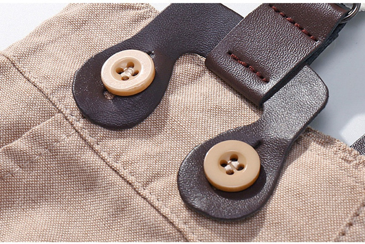 OONA Short-Sleeve Romper Short Suit with Hat, detailed close-up of the beige fabric, brown leather straps, and beige buttons.