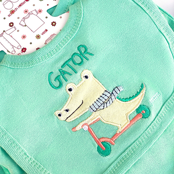 Generic Alligator Layette Set 8 Piece, light green baby bib with embroidered alligator riding a scooter and the word 'GATOR' on it.