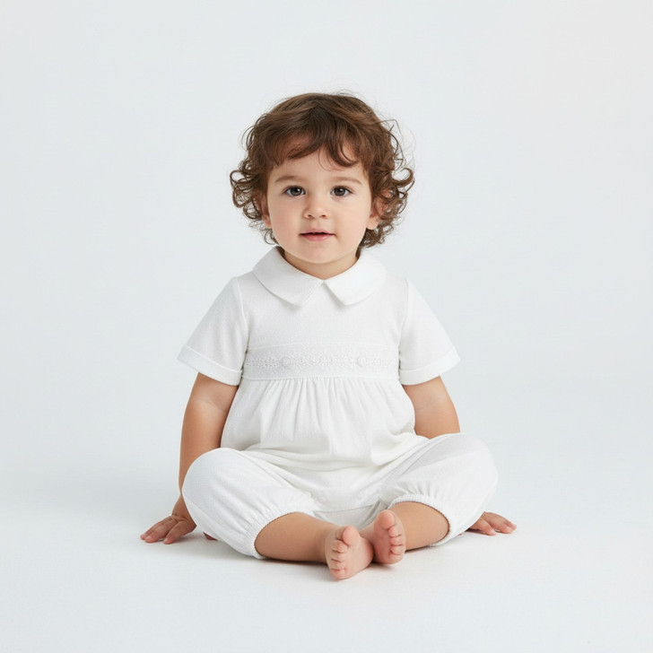Minnie Me Tommy Christening White Romper, adorable young child sitting on the white background in a white Christening romper with a Peter Pan collar.