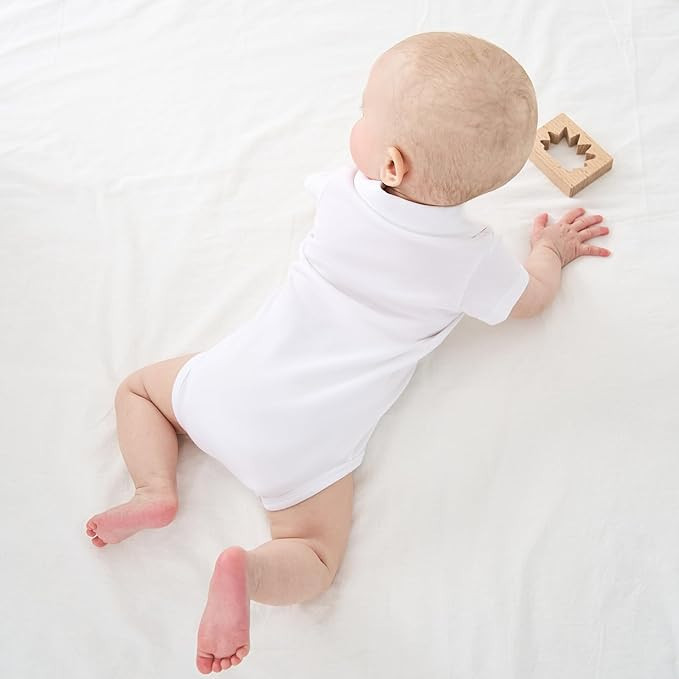 Minnie Me Cotton Romper Neutral, a baby lying on a white surface wearing a white romper and playing with a wooden toy.