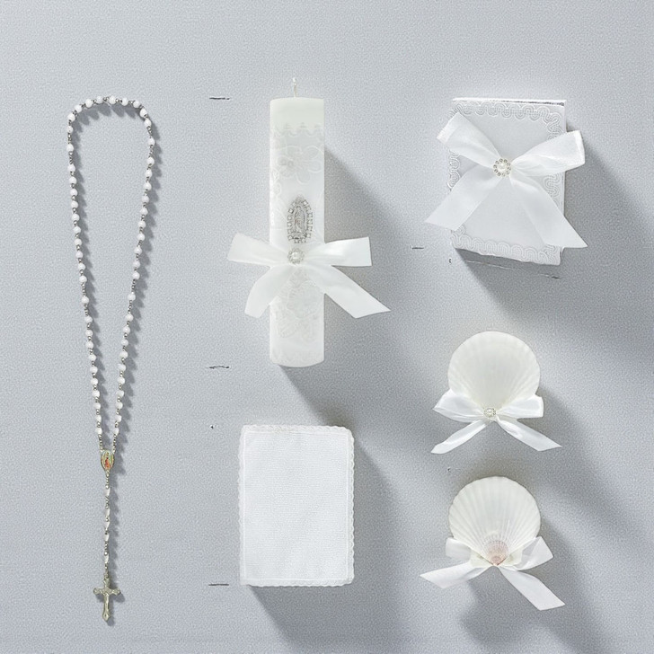 Minnie Me White 5 PCS Baptism Kit, image shows a white rosary with a cross, a white baptism candle decorated with lace and a bow, a small white gift box with a bow, and two white shell-shaped items decorated with bows for a baptism ceremony.