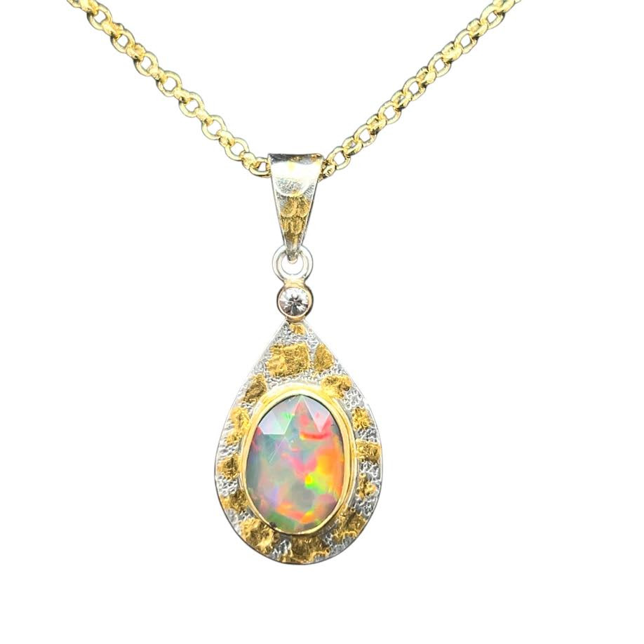Welo Opal Pendant and Sapphire with 22k Gold. I cut this very bright and gemmy opal from a parcel of Ethiopian opal. Has multi-flashes of all the colors of the sky with blue, green, orange, red and yellow. This opal has multiple facets on the face that reflect a kaleidoscope of colors. Set in a 22K gold bezel with 22K gold accents and a white sapphire accent set in 14K gold filled setting. Base layer is textured sterling silver and comes with an 18 inch 14K gold filled chain.
Opals naturally contain 4-10% water. It is NOT recommended to shower, wash, or expose opals to long periods of water contact. 1”L by ¾ “ W.