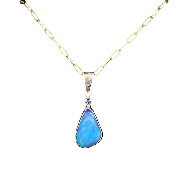 Welo Opal Pendant in 22K Gold and Silver. I cut this multi-colored opal from Ethiopia in a unique triangular drop design. This high quality opal is very bright and has all the colors of the rainbow.  The colors run along a vertical seam creating a sheet of color.
Set in solid 22K gold bezel with a silver backing. I added a small light blue sapphire which creates a subtle sparkle of color that complements the opal colors. The bail is hand made with 22K gold Keumboo over silver and comes with a 14K gold filled chain and clasp. From the front view, all you see is gold.
Opals naturally contain 4-10% water. It is NOT recommended to shower, wash, or expose opals to long periods of water contact.