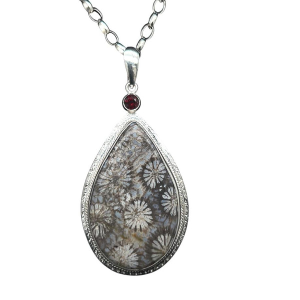 Petrified Coral Pendant with Garnet. I cut this unique design from a specimen of petrified coral from Indonesia. The details that were preserved in the skeletal structure are amazing. A Rhodolite Garnet from Africa act as a colorful contrast and the pendant is surrounded by a detailed gallery wire and different types of hand textures on the surround . 18’ Sterling Silver chain included. 1.5” L by 1” W.