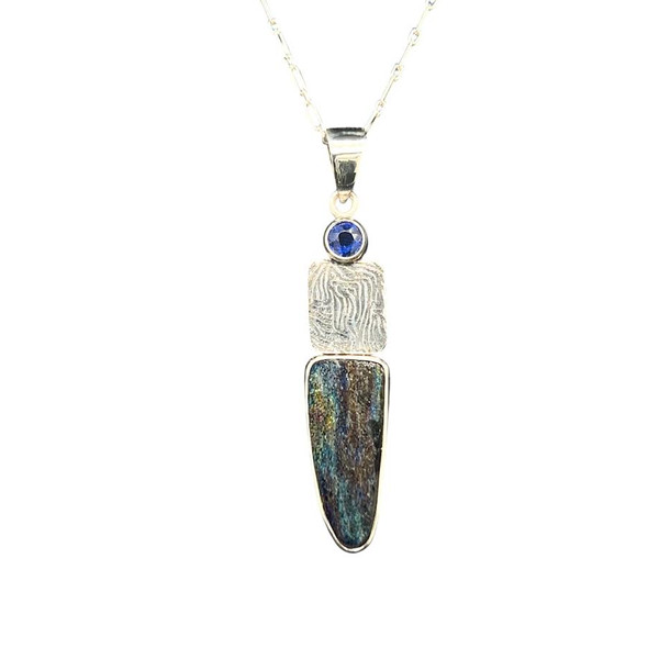 Rainbow Hematite with Iolite Pendant. This completely natural stone comes from a now closed mine from Brazil. Obviously this material is very rare and contains hematite crystals which naturally oxidize to form the intense colors. Set with a blue Iolite from Madagascar. 18” sterling silver chain included. 1” H by 0.5” W.