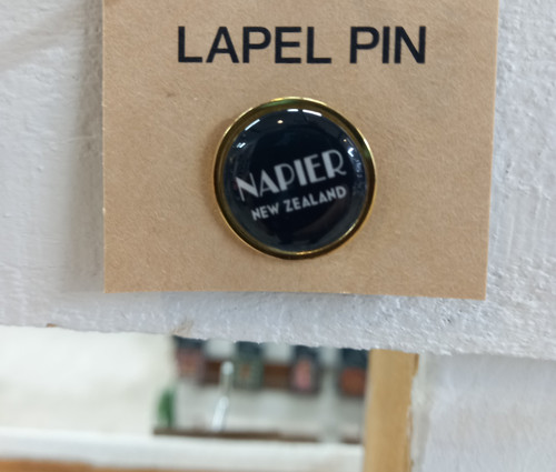 Napier New Zealand lapel pin with white Art Deco lettering on black and a gold-coloured edge, on display card