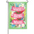 A green garden flag with the white text "World's Best Mom" on a pink ribbon surrounded by flowers.