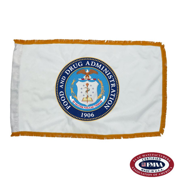 The indoor FDA flag is white and has 3 sides of gold fringe along the border. In the center is the agency’s seal, depicting a white shield and a bald eagle.