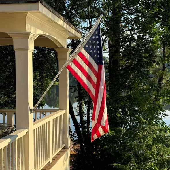 Photograph submitted by Mike Buffington. The American flag flown from a house-mounted pole in front of a forested lake.