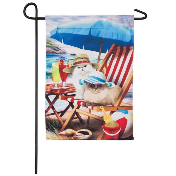 This flag features a scene of two white cats sitting on a beach chair on the beach. They are wearing floppy hats. There is a blue sun umbrella, beach ball, seashells, cocktails, and sand buckets.