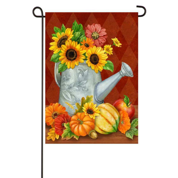 A red garden flag featuring a large watering can overflowing with sunflowers and various gourds.