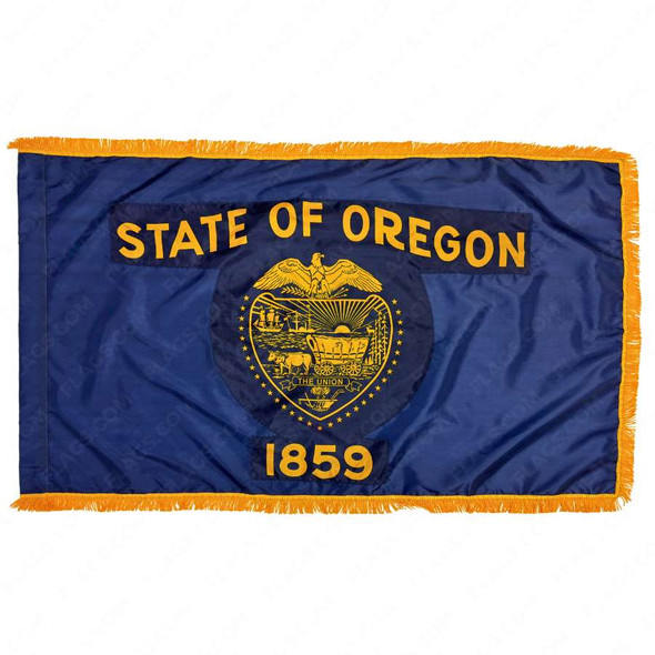 The indoor Oregon flag has 3 sides of gold fringe around the dark blue field. In the center is the state seal & the text “State of Oregon 1859”.