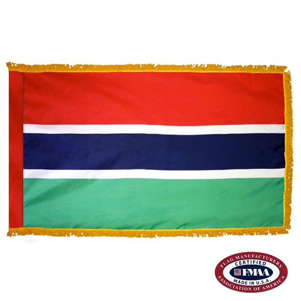 The indoor Gambia flag has 3 sides of gold fringe around a red, blue, and green tricolor. The blue stripe has white outlines above and below. FMAA Certified Made in America seal.