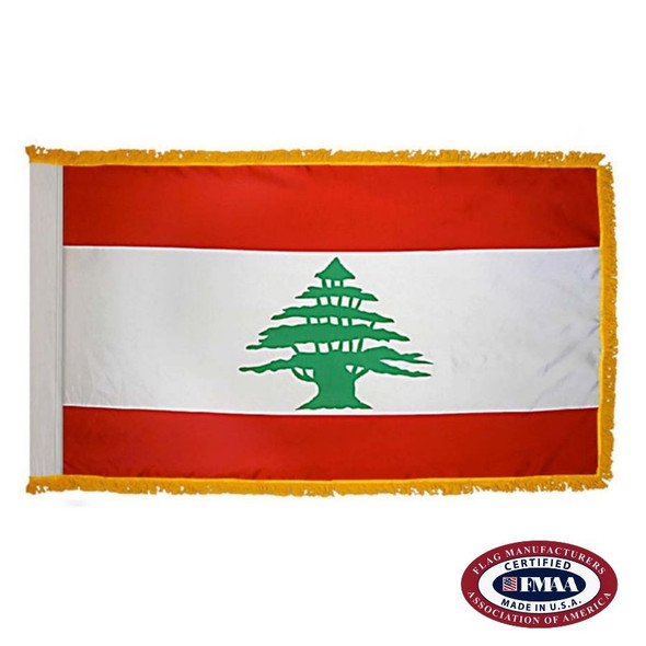 The indoor Lebanon flag has 3 sides of gold fringe around 3 red and white stripes. In the center of the wider white stripe is a cedar tree. FMAA Certified Made in America seal.