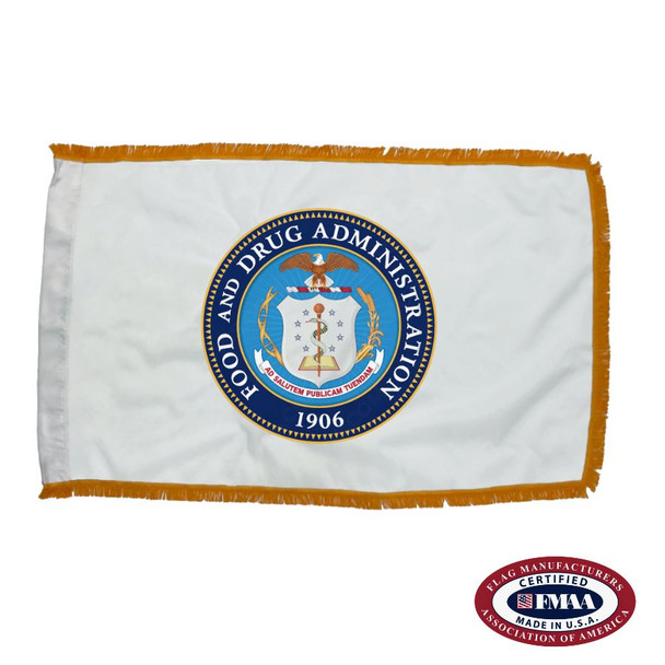 The indoor FDA flag is white and has 3 sides of gold fringe along the border. In the center is the agency’s seal, depicting a white shield and a bald eagle.