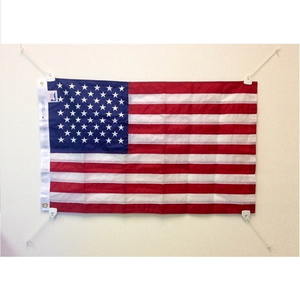 An American flag with a grommet clip attached in each corner and hung horizontally on a white wall using string.