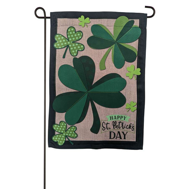 A garden flag depicting several green clovers on a beige background above the text "Happy St. Patrick's Day".