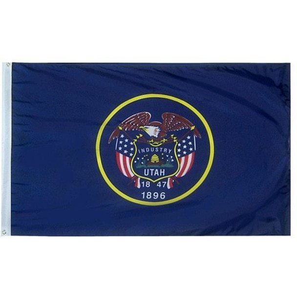 A blue Utah flag with a seal in the center. Six arrows, a beehive, sego lilies, and the text “Industry, Utah, 1847” are shown on the seal, framed by two US flags. A bald eagle perches at the top, and the text “1896” is written below the seal.