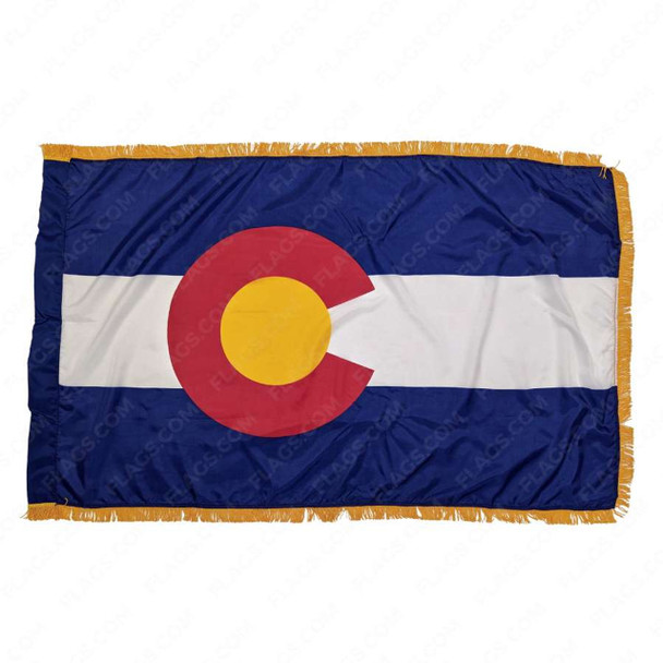 The indoor Colorado flag has a pole sleeve and 3 edges of gold fringe surrounding the blue & white striped flag, with a red C in the center.