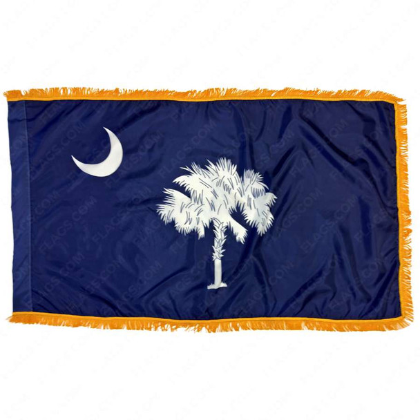 The indoor South Carolina flag has gold fringe around the dark blue field. In the center is a palmetto tree & in the top left is a crescent moon.