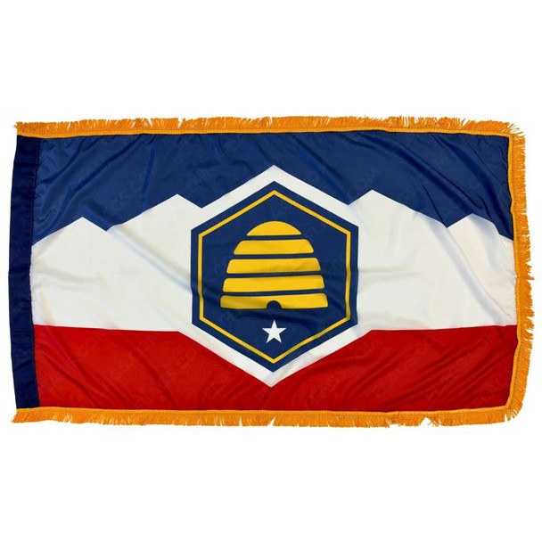 The indoor Utah flag has gold fringe around the blue, white, & red design. In the center is a yellow beehive in a blue hexagon.