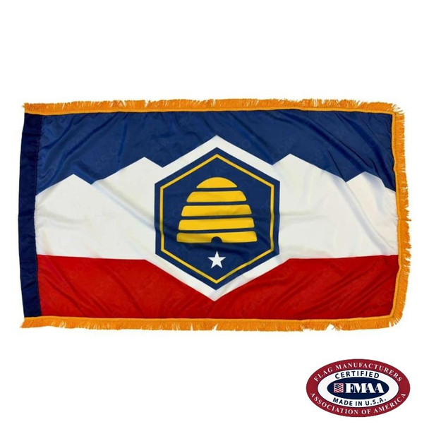 The indoor Utah flag has gold fringe around the blue, white, & red design. In the center is a yellow beehive in a blue hexagon. FMAA Certified Made in America seal.