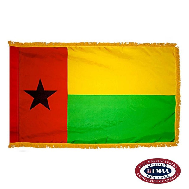 The indoor Guinea-Bissau flag has 3 sides of gold fringe around 2 yellow and green stripes with a red field on the left with a black star. FMAA Certified Made in America seal.