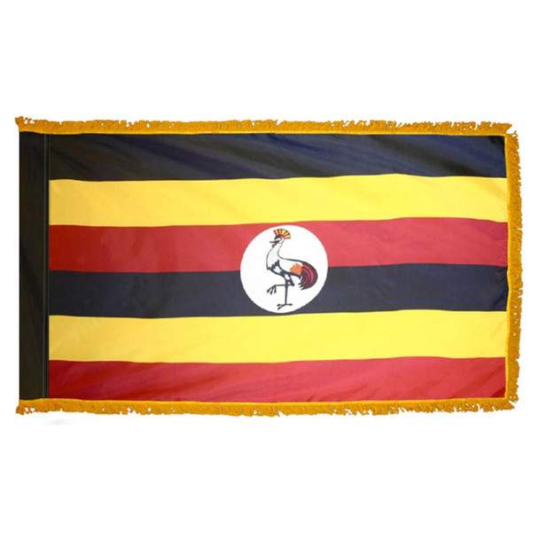 The indoor Uganda flag has 3 sides of gold fringe around 6 black, yellow, and red stripes. In the center is a white circle with a crane.