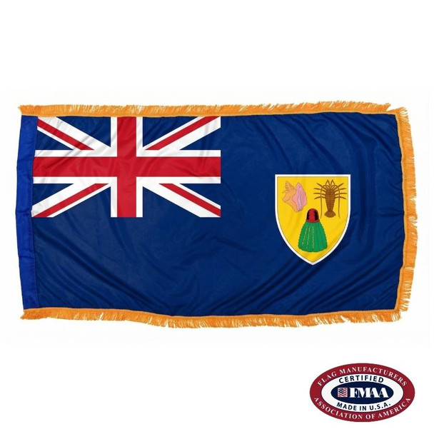 The indoor Turks & Caicos flag has 3 sides of gold fringe around a blue field with a Union Jack in the canton & a coat of arms on the right. FMAA Certified Made in America seal.