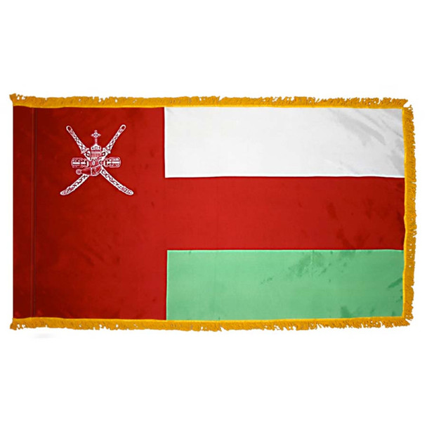 The indoor Oman flag has 3 sides of gold fringe around a white, red, and green tricolor. On the left is a red field with the national emblem.
