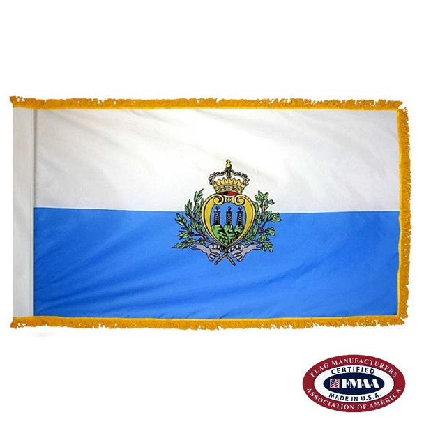 The indoor San Marino flag has 3 sides of gold fringe around a horizontal white and blue bicolor with a coat of arms in the center. FMAA Certified Made in America seal.