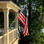 Photograph submitted by Mike Buffington. The American flag is being flown from a house-mounted pole in front of a forested lake.