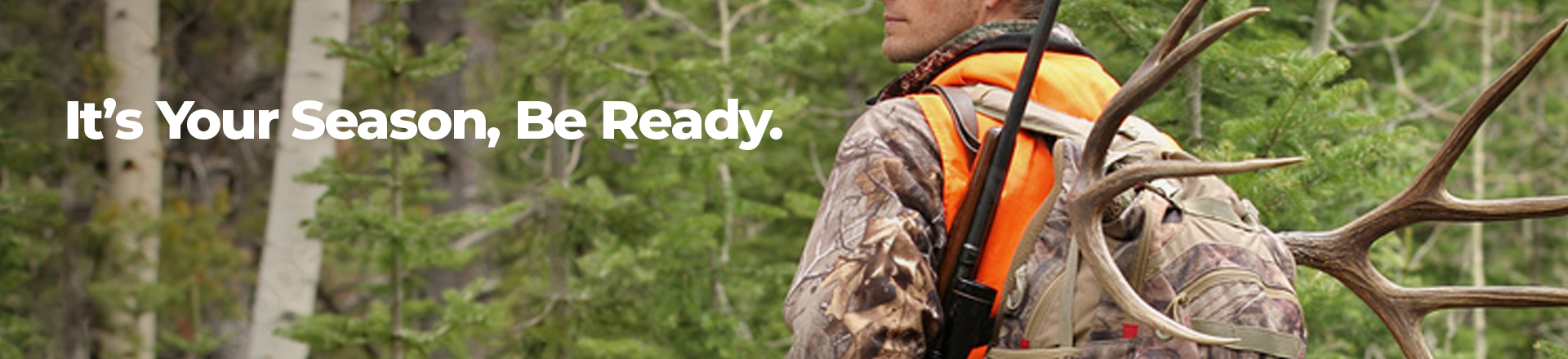 Hunter in woods wearing camo coat and orange safety vest.