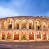 The historic Roman amphitheater of Verona lit up at twilight, showcasing the arches and weathered stones with a warm, inviting glow.