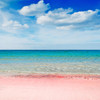 Scenic view of the Spiaggia Rosa, famous for its unique pink sands, with clear turquoise waters of the Mediterranean Sea under a bright blue sky dotted with fluffy white clouds.