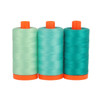 Three large spools of Aurifil Capri 50wt Egyptian cotton thread in coordinating shades of aqua on a white background.