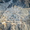 Aerial view of Carrara marble quarry in Italy, showcasing the striking terraced landscape with white stone and winding dirt roads.