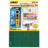 The image displays the OLFA Premium Quilt Making Kit, including a 45mm rotary cutter with a black and yellow handle, a frosted acrylic ruler with grid lines, and a green double-sided rotary mat with yellow grid lines. The packaging features the OLFA logo and product names, with descriptions in multiple languages