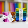 2 sets of Atomic 2½ inch fabric strips jelly roll by Andover tied with Morris Works ribbons against a background of fabric rolls.