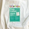 A close-up of Matilda's Own extra wide 100% Cotton Quilt Wadding with its green product label placed on top. The label highlights key features, including "100% Cotton," "Machine Washable," and "2.4m Width." It also states that the wadding is "Made in Australia" and provides a low loft for a traditional quilting finish. A section on the label explains the benefits of pure cotton wadding, mentioning its breathability, softness, and suitability for heirloom quilting. Care instructions and key product details are listed at the bottom, along with the Victorian Textiles logo and website information. The wadding itself appears soft, off-white, and textured.