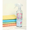 The June Tailor Quilter's Starch Savvy spray bottle, positioned in front of neatly stacked quilting fabrics in various colors, ready for use to stiffen and prepare fabric for precise quilting work.