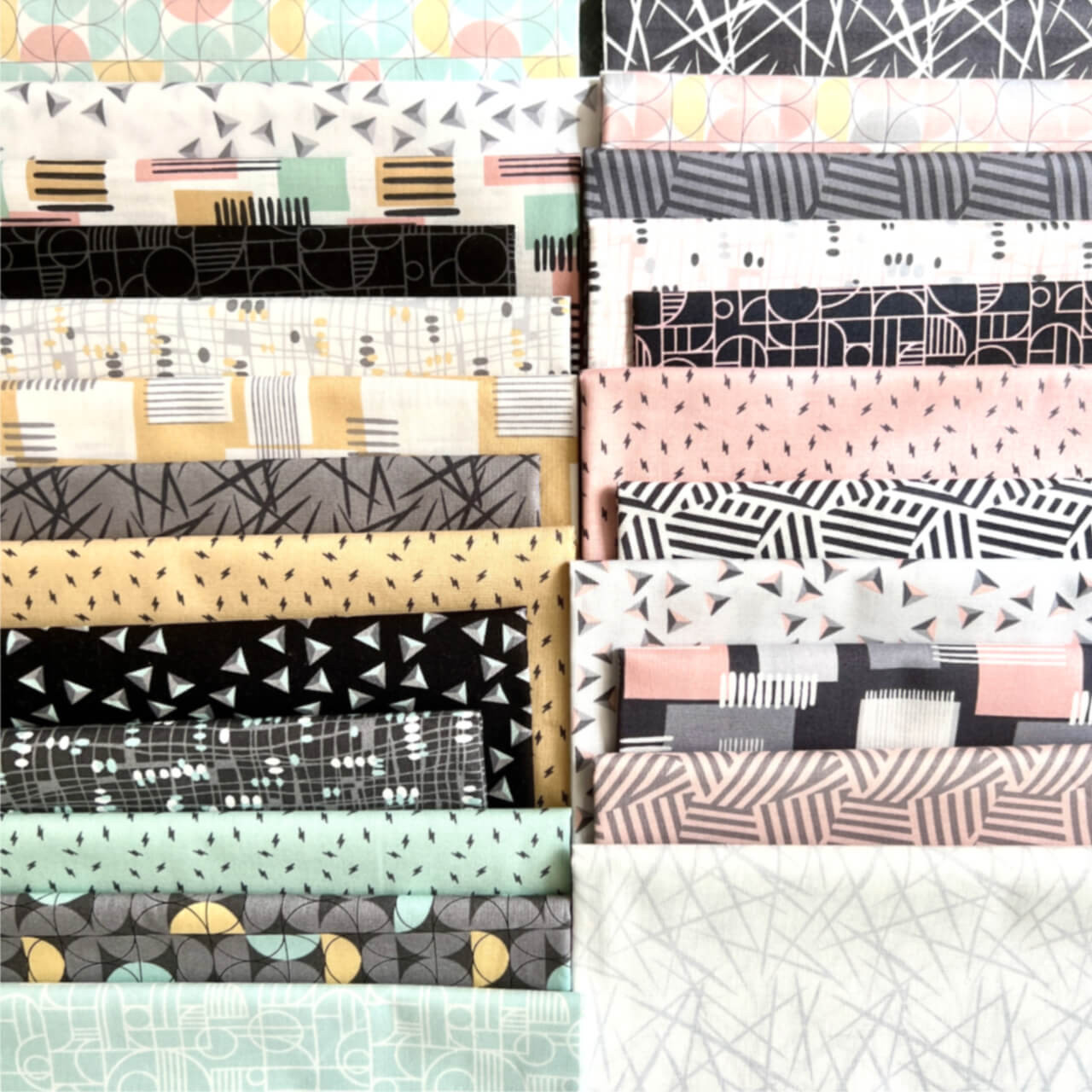 The image shows a collection of cascading fabric squares with geometric patterns in black, grey, mustard, mint, and pink. Bold shapes contrast with subtle designs, presenting a textured and varied assortment from the Rancho Relaxo series.