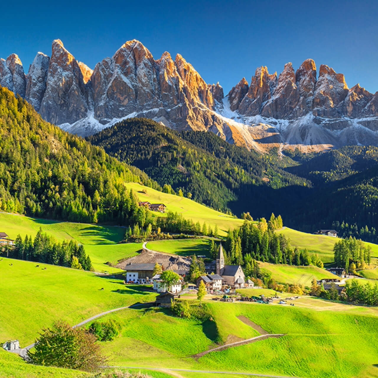 Breathtaking view of the Dolomite mountains with snow-capped peaks towering over lush green Alpine meadows and a small village with traditional houses in the valley.