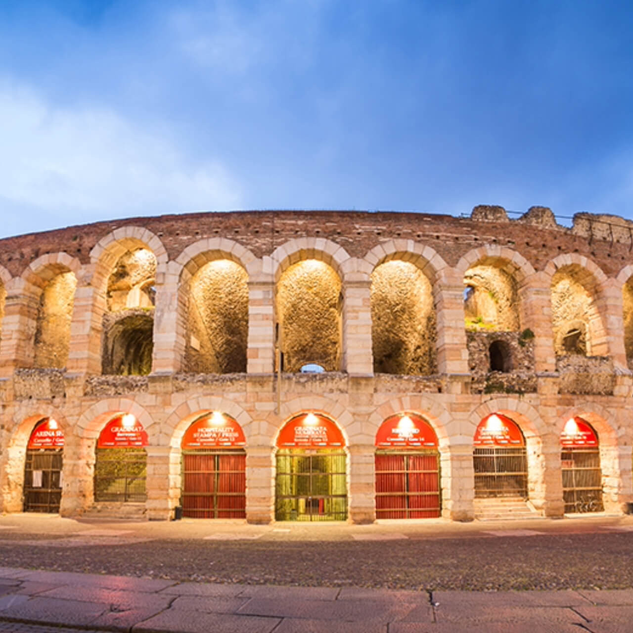 The historic Roman amphitheater of Verona lit up at twilight, showcasing the arches and weathered stones with a warm, inviting glow.